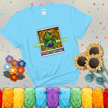 Retro-styled illustration of a glamorous green frog in a sparkly outfit, labeled "Frogette the Ripper" with the phrase “Oops! I frogged it again” below, referencing both crochet and pop culture showing a light blue tee with grey sunflower background