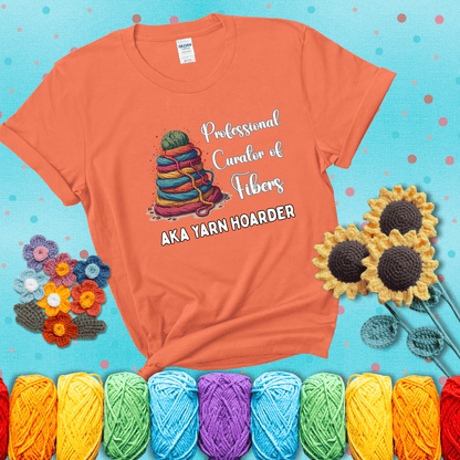 Pyramid of rainbow yarn topped with green ball; text reads “Professional Curator of Fibers AKA Yarn Hoarder,” a playful shirt for serious stashers showing a light orange tee with a teal sunflower background