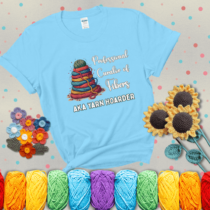 Pyramid of rainbow yarn topped with green ball; text reads “Professional Curator of Fibers AKA Yarn Hoarder,” a playful shirt for serious stashers showing a light blue tee with grey sunflower background