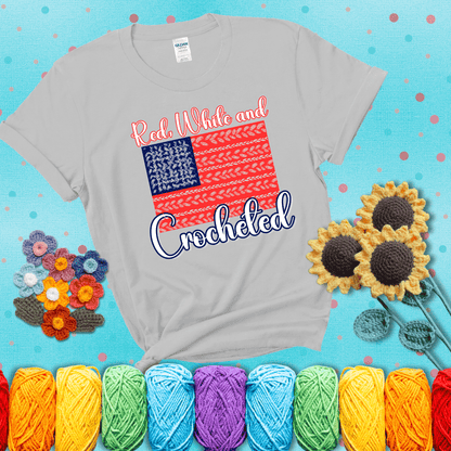 Patriotic crochet-themed American flag design with red and white yarn stitches forming the stripes and blue and white stitches as stars, showing a light grey tee with a teal sunflower background
