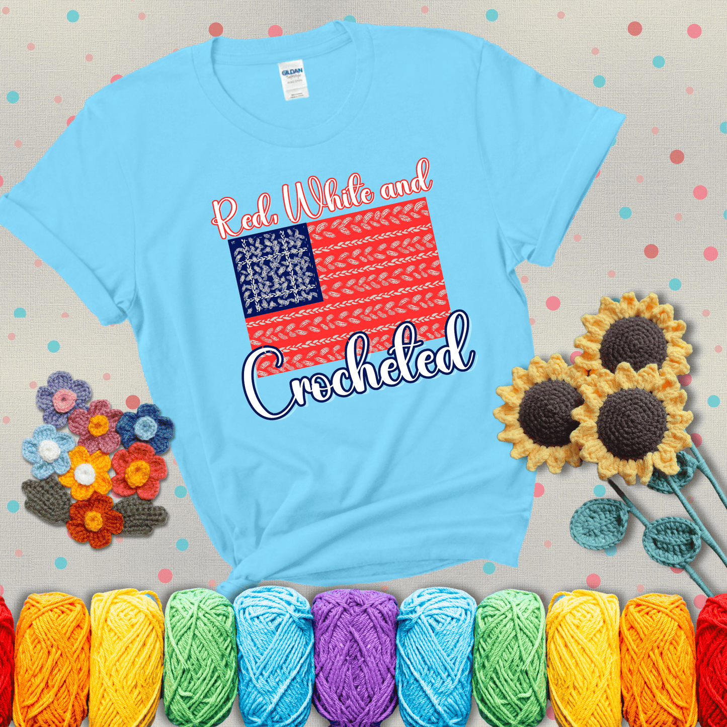 Patriotic crochet-themed American flag design with red and white yarn stitches forming the stripes and blue and white stitches as stars, showing a light blue tee with grey sunflower background
