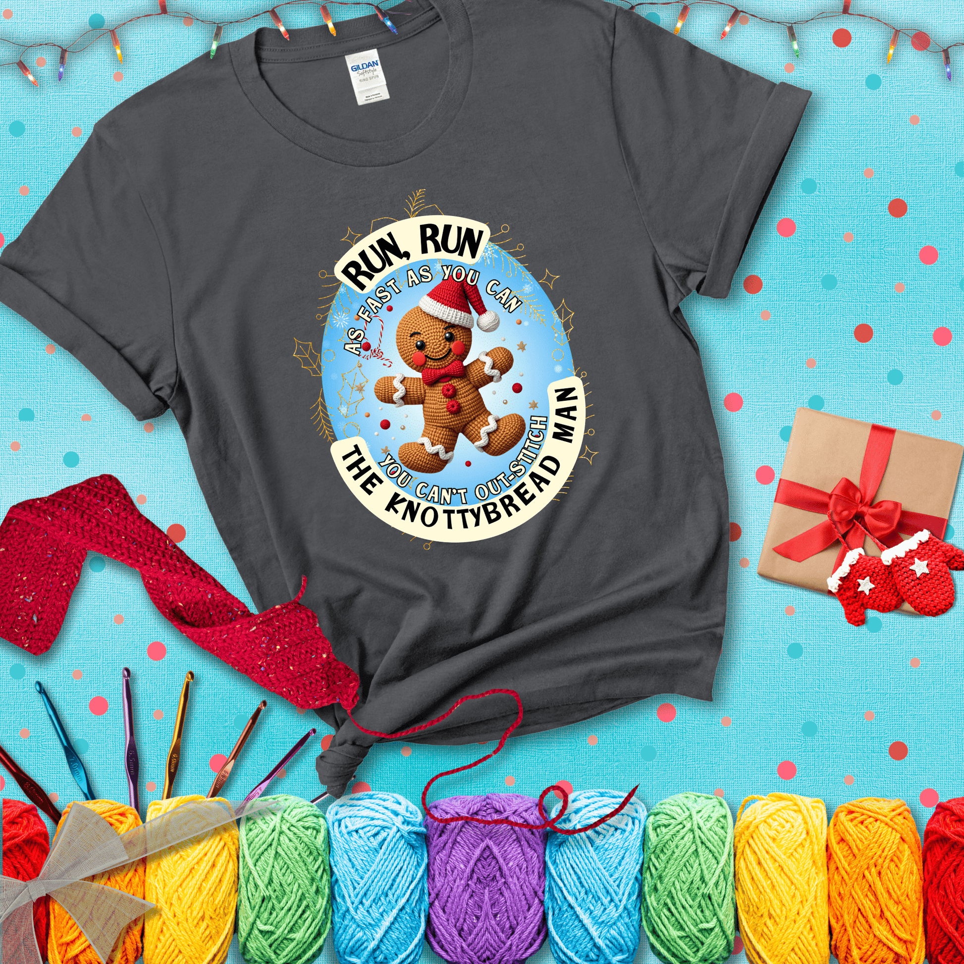 Cute crocheted gingerbread man in Santa hat with playful text: “Run, Run As Fast As You Can, You Can’t Out-Stitch the Knottybread Man.” A festive crochet pun shirt, showing a dark grey tee with a festive Christmas background