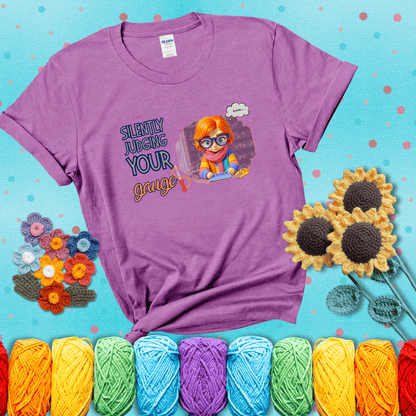 A serious-looking crocheter with rainbow clothes, big glasses, and a tape measure silently examines their stitches under the phrase “Silently judging your gauge” showing a light purple tee with a teal sunflower background