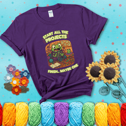 A wide-eyed crochet frog sits tangled in yarn with dozens of projects around, surrounded by chaos and “new project” notes. Caption reads “Start all the projects, finish... maybe one” showing a purple tee with a teal sunflower background