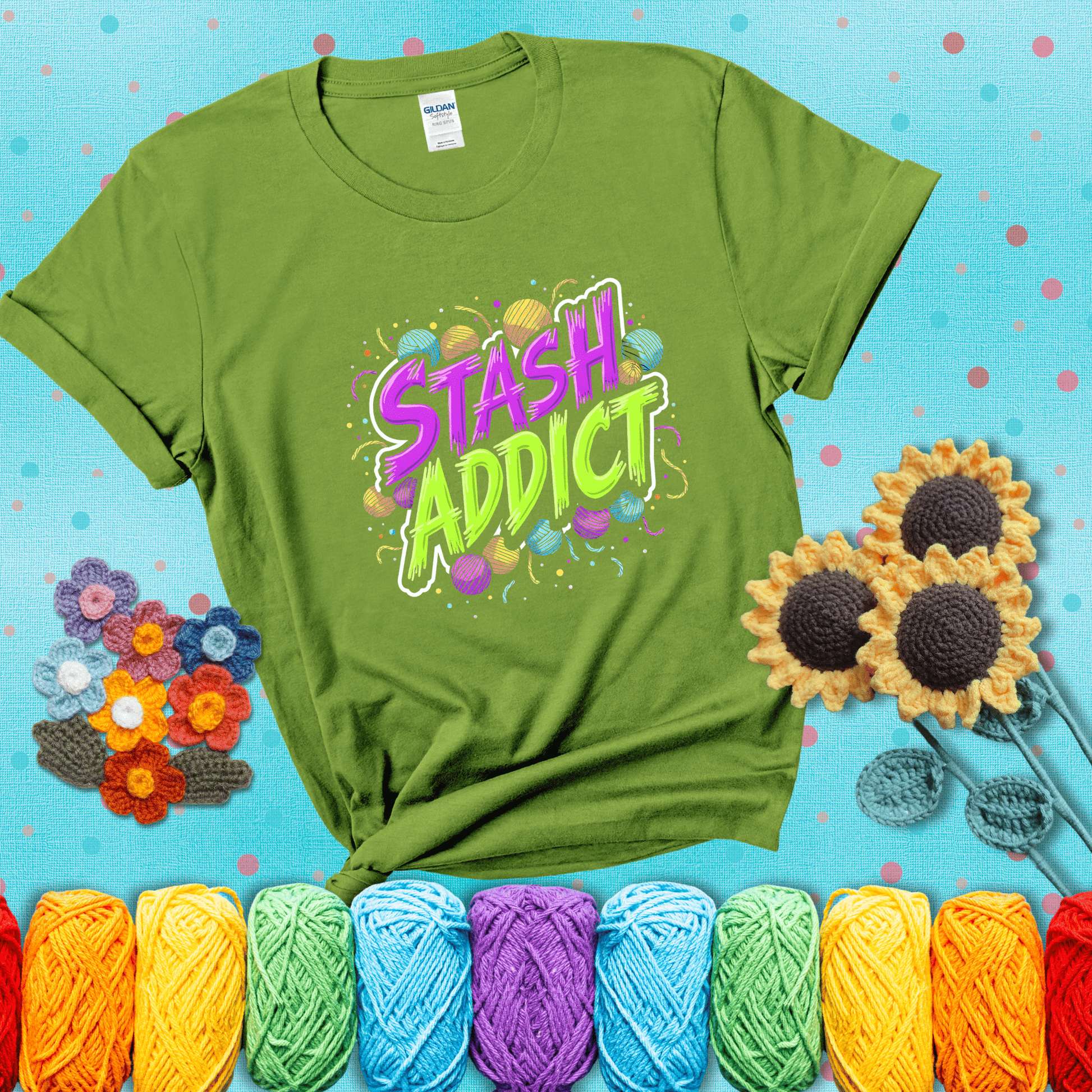 Bold neon text reading "Stash Addict" surrounded by colorful yarn balls and festive confetti on a neutral background showing a bright green tee with a teal sunflower background