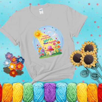 A happy spring garden scene with a sunbeam, flowers, and a pink yarn ball on a mushroom, with the quote "Surround yourself with yarn, knot negativity," showing a light grey tee with a teal sunflower background