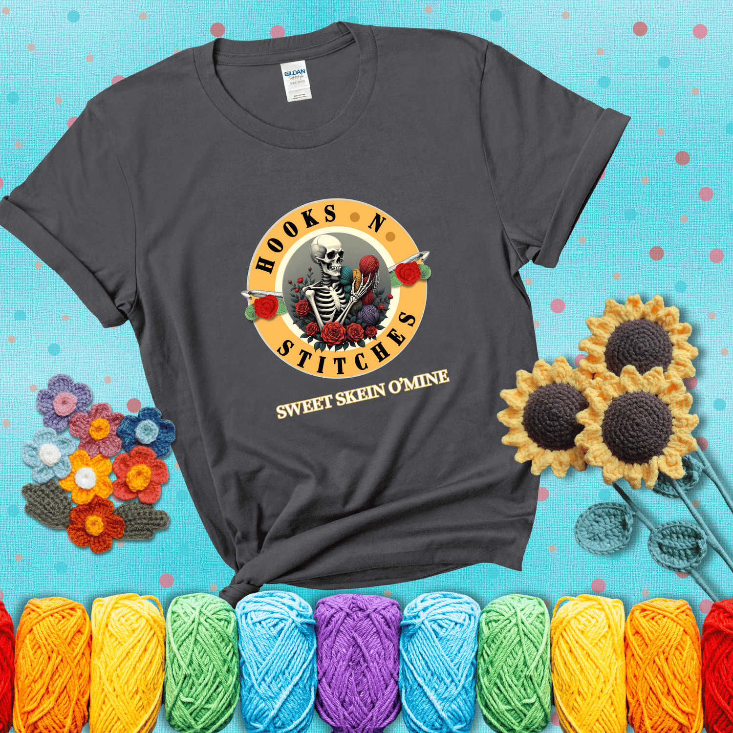 A skeleton holding colorful yarn, surrounded by roses, framed in a circular logo-style design that says “Hooks 'N Stitches” and “Sweet Skein O’Mine,” with crochet hooks piercing through showing a dark grey tee with a teal sunflower background