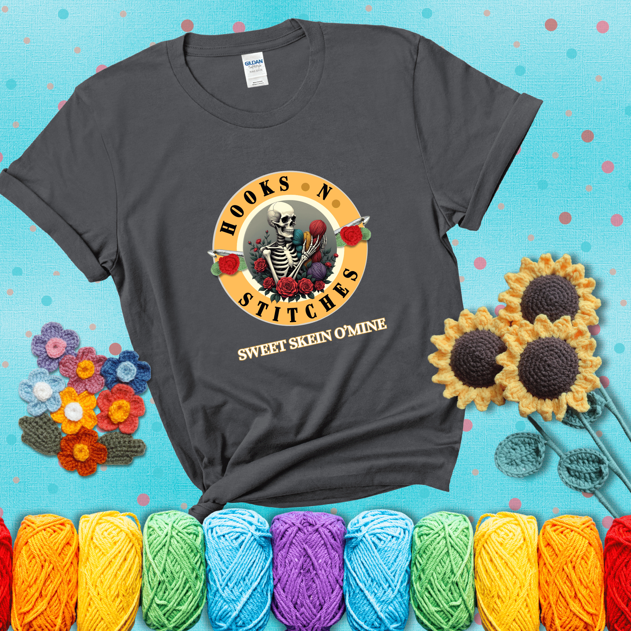 A skeleton holding colorful yarn, surrounded by roses, framed in a circular logo-style design that says “Hooks 'N Stitches” and “Sweet Skein O’Mine,” with crochet hooks piercing through showing a dark grey tee with a teal sunflower background