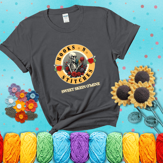 A skeleton holding colorful yarn, surrounded by roses, framed in a circular logo-style design that says “Hooks 'N Stitches” and “Sweet Skein O’Mine,” with crochet hooks piercing through showing a dark grey tee with a teal sunflower background
