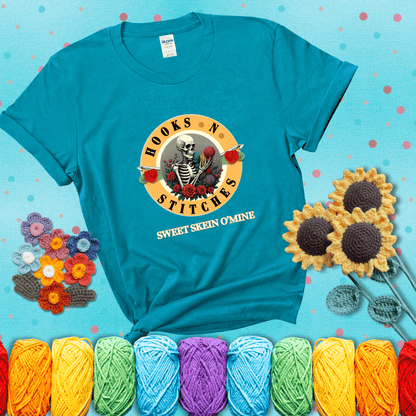 A skeleton holding colorful yarn, surrounded by roses, framed in a circular logo-style design that says “Hooks 'N Stitches” and “Sweet Skein O’Mine,” with crochet hooks piercing through showing a blue-green tee with a teal sunflower background