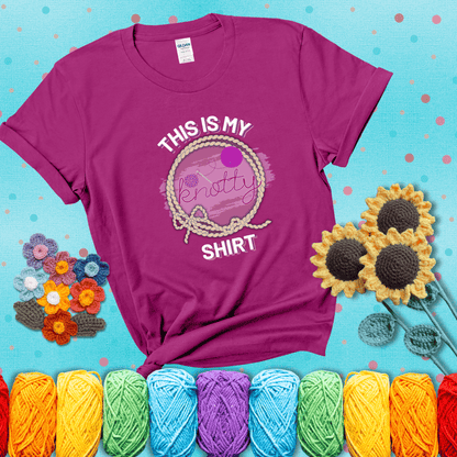 A playful design with the phrase "This is my knotty shirt" inside a rope circle, featuring a yarn ball and a crochet hook forming the word "knotty" showing a magenta tee with a teal sunflower background