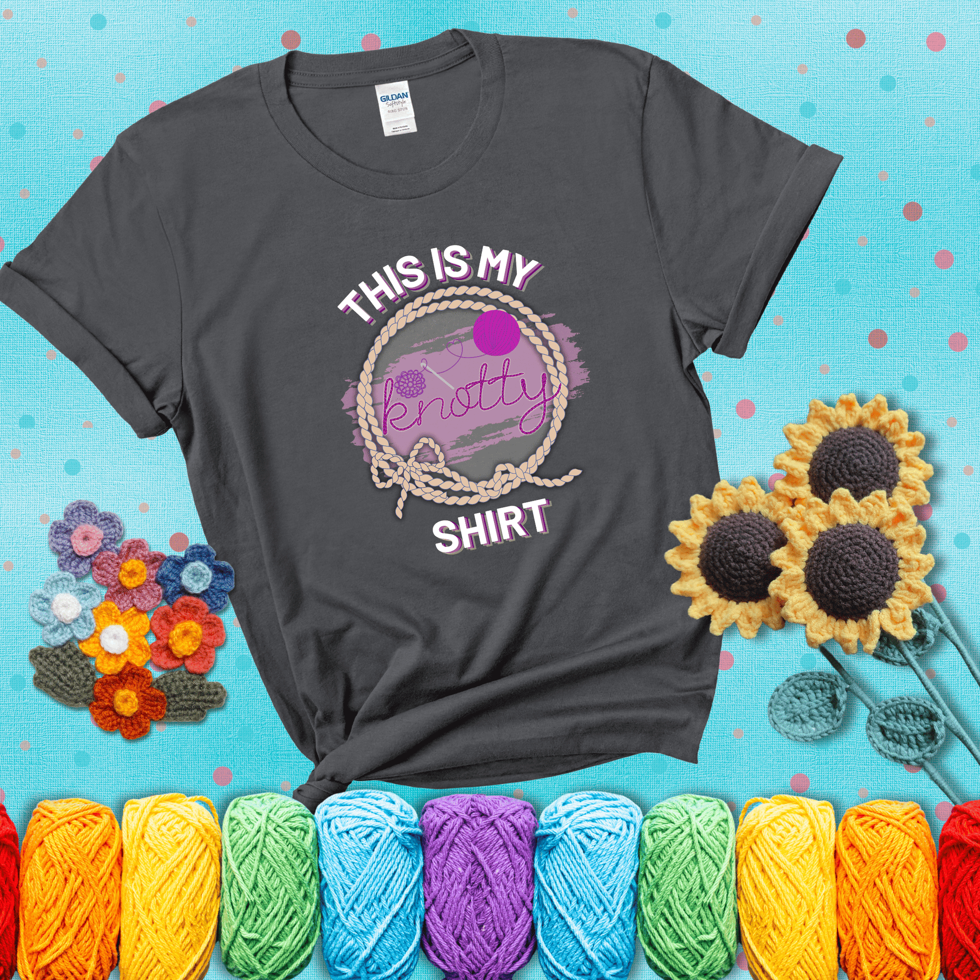 A playful design with the phrase "This is my knotty shirt" inside a rope circle, featuring a yarn ball and a crochet hook forming the word "knotty" showing a dark grey tee with a teal sunflower background