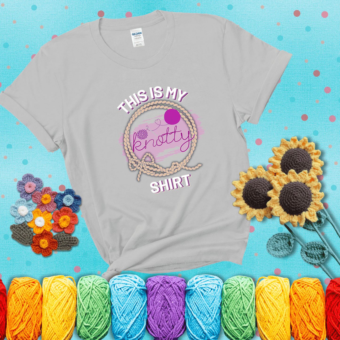 A playful design with the phrase "This is my knotty shirt" inside a rope circle, featuring a yarn ball and a crochet hook forming the word "knotty" showing a light grey tee with a teal sunflower background