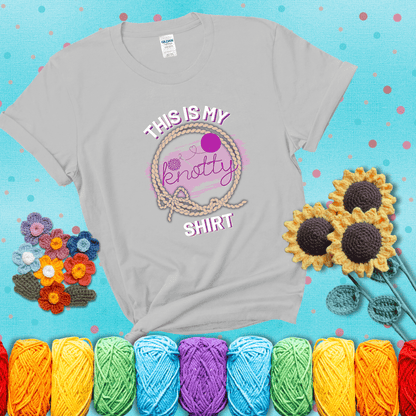 A playful design with the phrase "This is my knotty shirt" inside a rope circle, featuring a yarn ball and a crochet hook forming the word "knotty" showing a light grey tee with a teal sunflower background