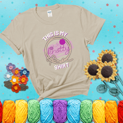 A playful design with the phrase "This is my knotty shirt" inside a rope circle, featuring a yarn ball and a crochet hook forming the word "knotty" showing a beige tee with a teal sunflower background