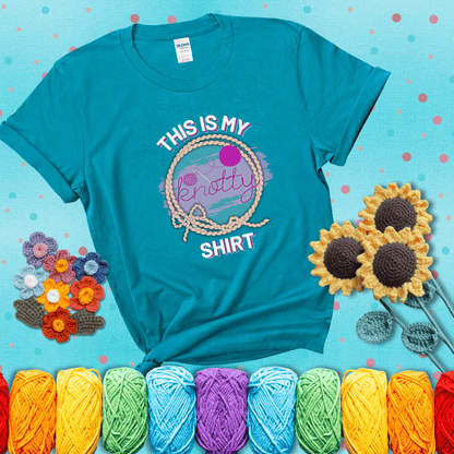 A playful design with the phrase "This is my knotty shirt" inside a rope circle, featuring a yarn ball and a crochet hook forming the word "knotty" showing a blue-green tee with a teal sunflower background