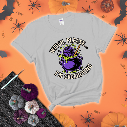 Put a spell on your stash Design reads 'Witch, Please… I’m Crocheting,' perfect crochet gift for yarn lovers showing a light grey tee with a festive Halloween background