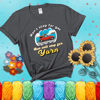 Woman joyfully driving a red convertible overflowing with yarn balls, paired with bold retro lettering and a playful slogan showing a dark grey tee with a teal sunflower background