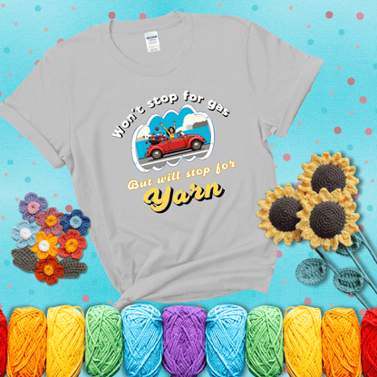Woman joyfully driving a red convertible overflowing with yarn balls, paired with bold retro lettering and a playful slogan showing a light grey tee with a teal sunflower background