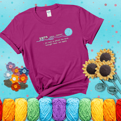 A definition-style graphic showing the word "yarn" as a noun, with the definition “An item to which the term ‘enough’ does not apply,” and a ball of blue yarn with a loose strand showing a magenta tee with a teal sunflower background