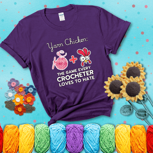 Cartoon chicken inside a yarn ball with crochet circle background. Text reads: “Yarn Chicken: The Game Every Crocheter Loves to Lose.” A fun and relatable tee for fiber artists who like to live on the edge, showing a purple tee with a teal sunflower background