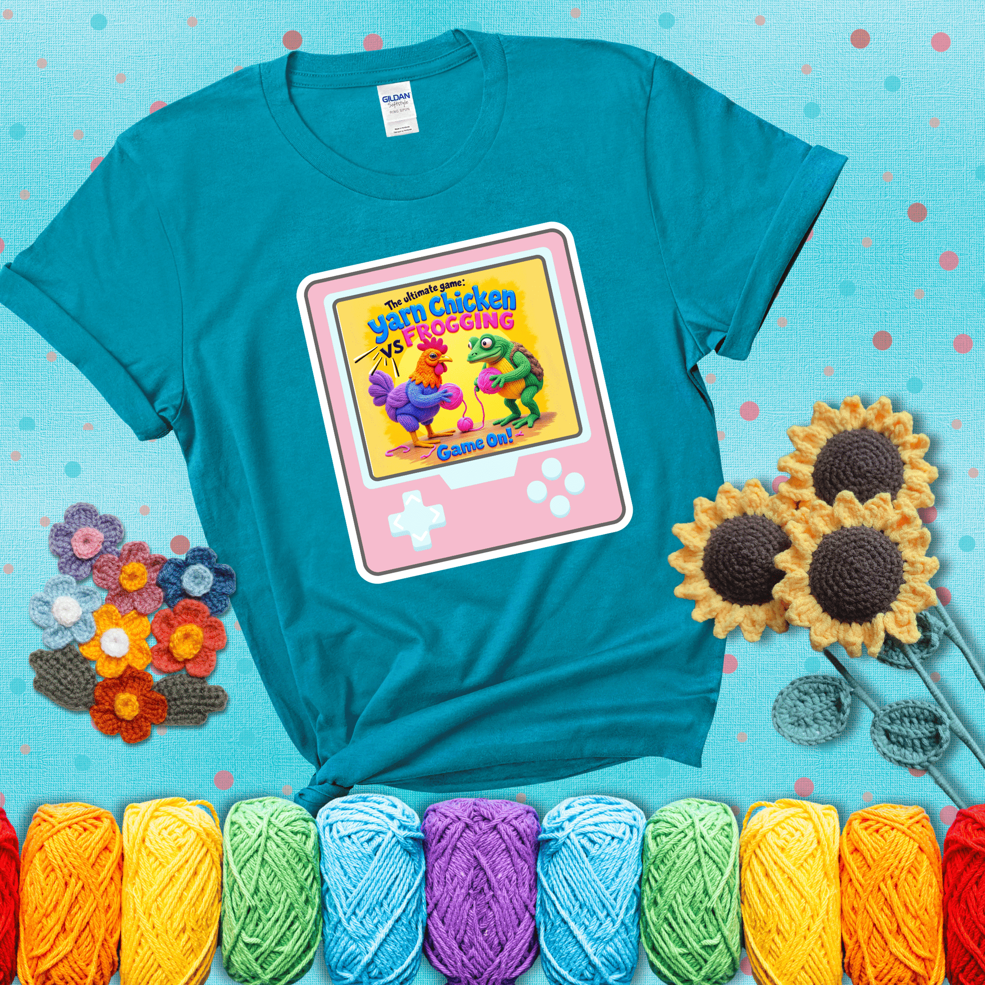 A colorful chicken and frog holding pink yarn face off inside a retro handheld game screen with the title “The ultimate game: Yarn Chicken vs. Frogging – Game On!” showing a blue-green tee with a teal sunflower background