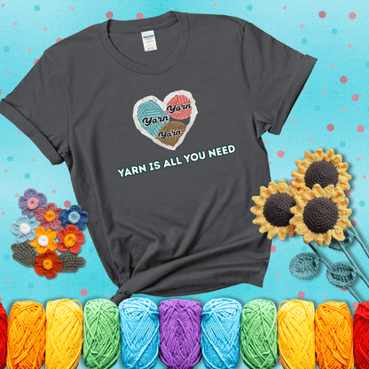 Heart made of yarn textures labeled “Yarn” in different colors above the phrase “Yarn is all you need” in bold retro type, showing a dark grey tee with a teal sunflower background