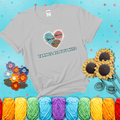 Heart made of yarn textures labeled “Yarn” in different colors above the phrase “Yarn is all you need” in bold retro type, showing a light grey tee with a teal sunflower background