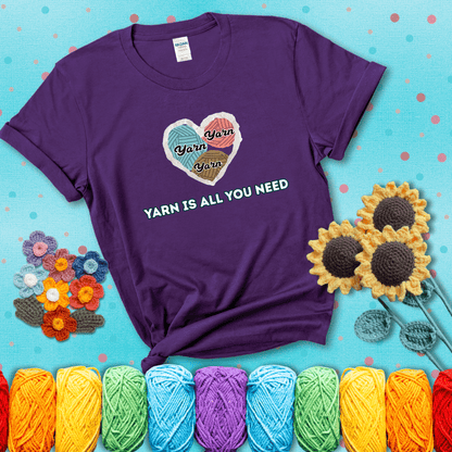 Heart made of yarn textures labeled “Yarn” in different colors above the phrase “Yarn is all you need” in bold retro type, showing a purple tee with a teal sunflower background