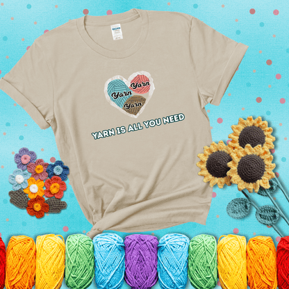 Heart made of yarn textures labeled “Yarn” in different colors above the phrase “Yarn is all you need” in bold retro type, showing a beige tee with a teal sunflower background