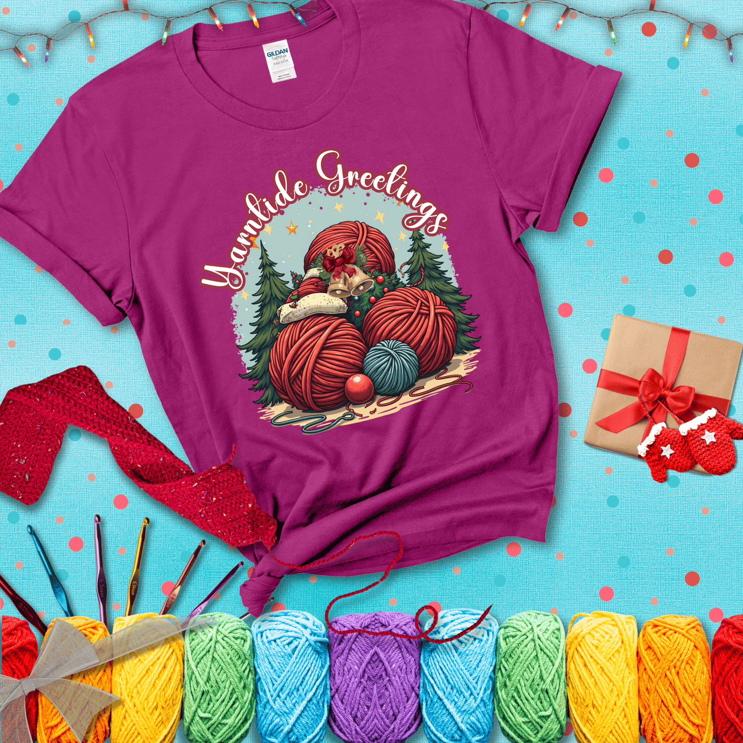 Pile of colorful yarn balls with bells, bows, and trees, with the phrase “Yarntide Greetings.” Cozy and festive holiday crochet tee, showing a magenta tee with a festive Christmas background