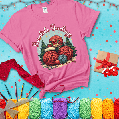 Pile of colorful yarn balls with bells, bows, and trees, with the phrase “Yarntide Greetings.” Cozy and festive holiday crochet tee, showing a pink tee with a festive Christmas background