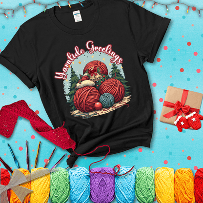 Pile of colorful yarn balls with bells, bows, and trees, with the phrase “Yarntide Greetings.” Cozy and festive holiday crochet tee, showing a black tee with a festive Christmas background