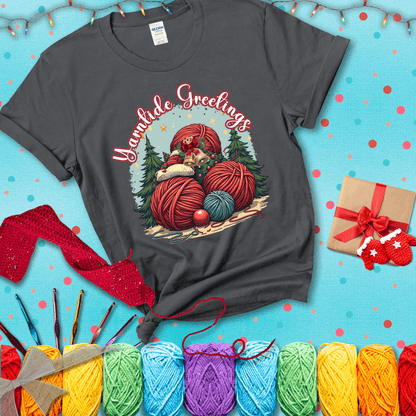 Pile of colorful yarn balls with bells, bows, and trees, with the phrase “Yarntide Greetings.” Cozy and festive holiday crochet tee, showing a dark grey tee with a festive Christmas background