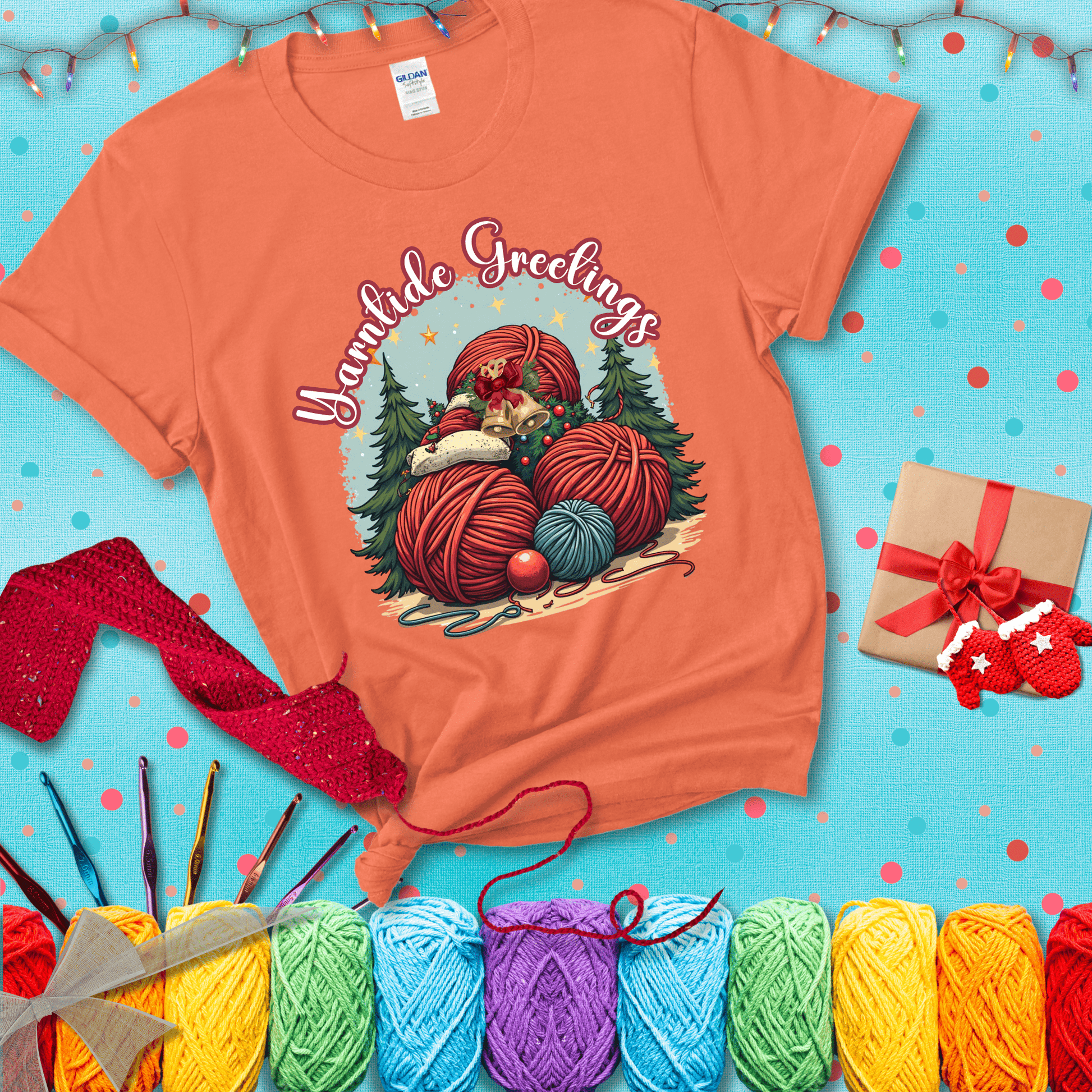 Pile of colorful yarn balls with bells, bows, and trees, with the phrase “Yarntide Greetings.” Cozy and festive holiday crochet tee, showing a light orange tee with a festive Christmas background