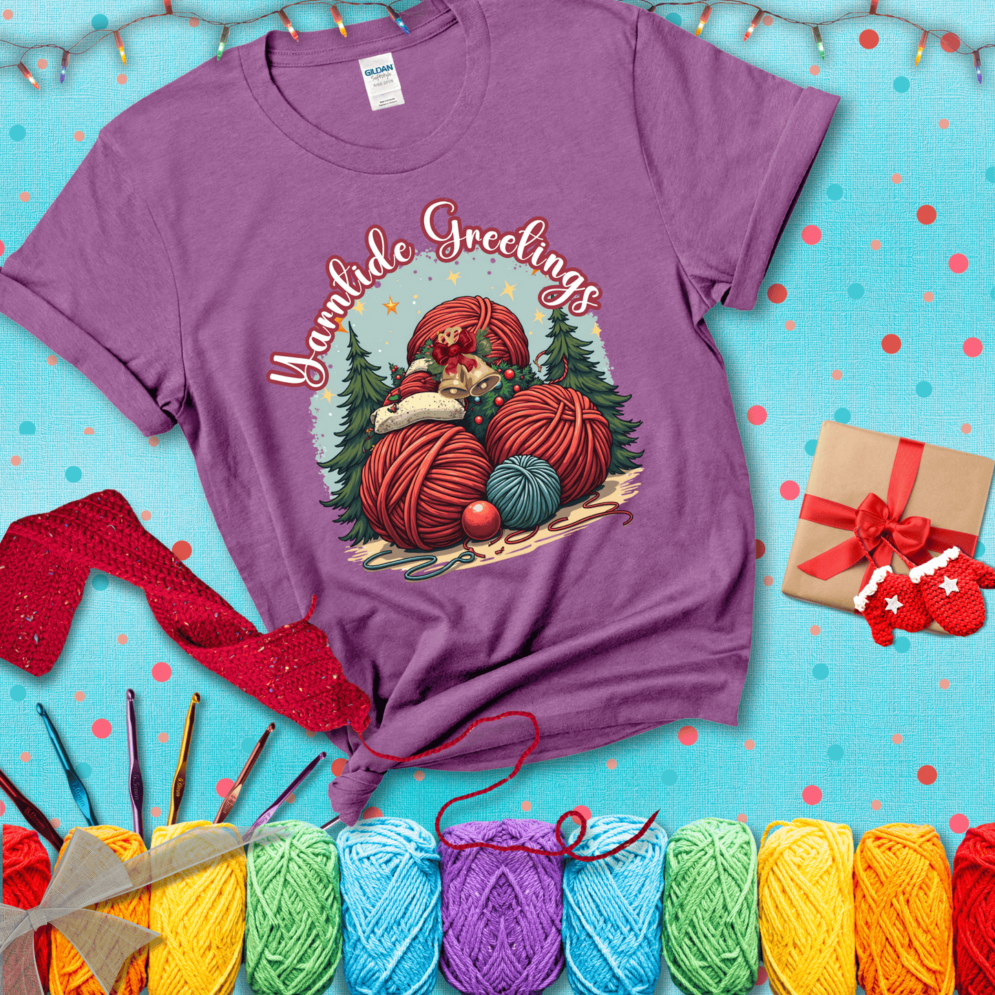 Pile of colorful yarn balls with bells, bows, and trees, with the phrase “Yarntide Greetings.” Cozy and festive holiday crochet tee, showing a light purple tee with a festive Christmas background