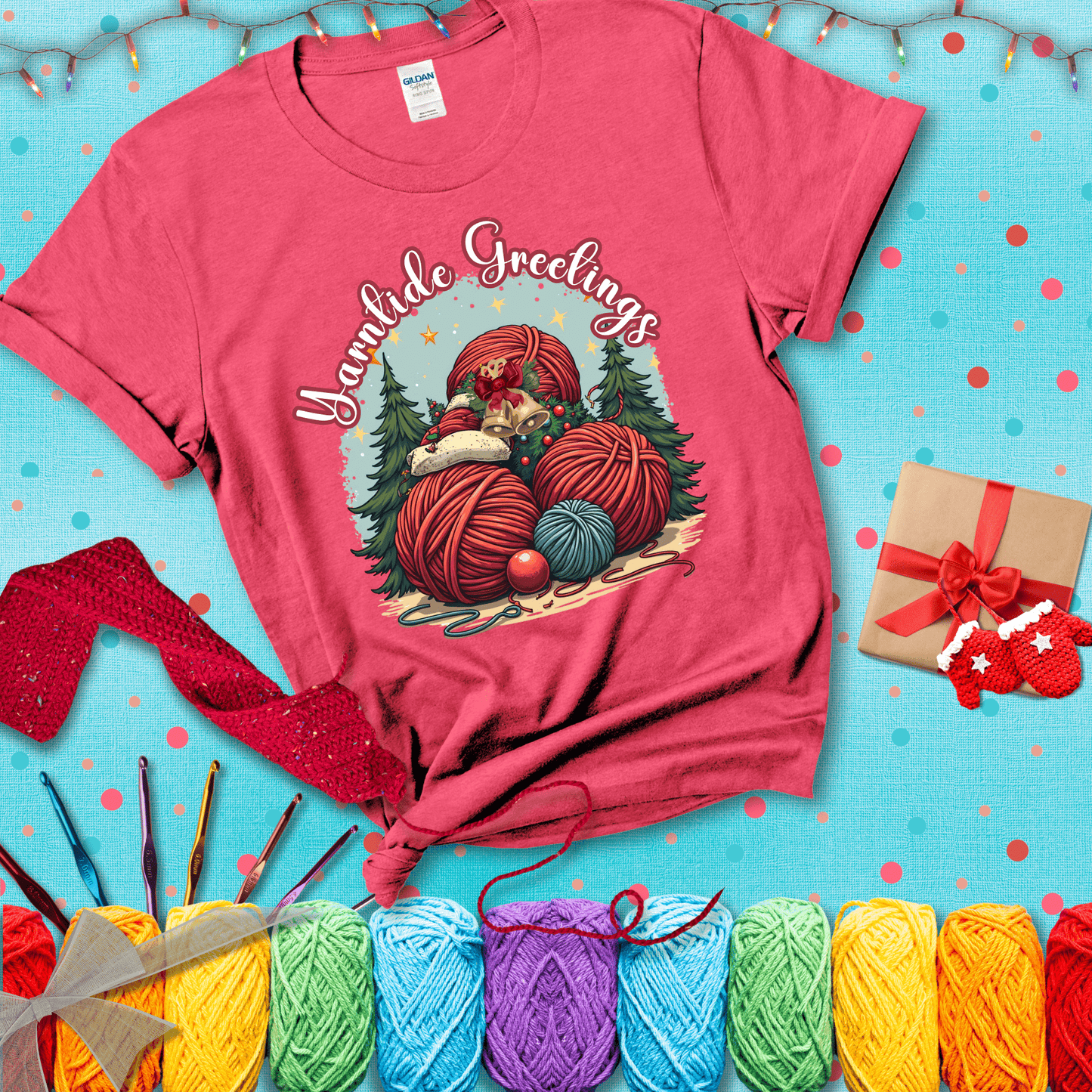 Pile of colorful yarn balls with bells, bows, and trees, with the phrase “Yarntide Greetings.” Cozy and festive holiday crochet tee, showing a light red tee with a festive Christmas background