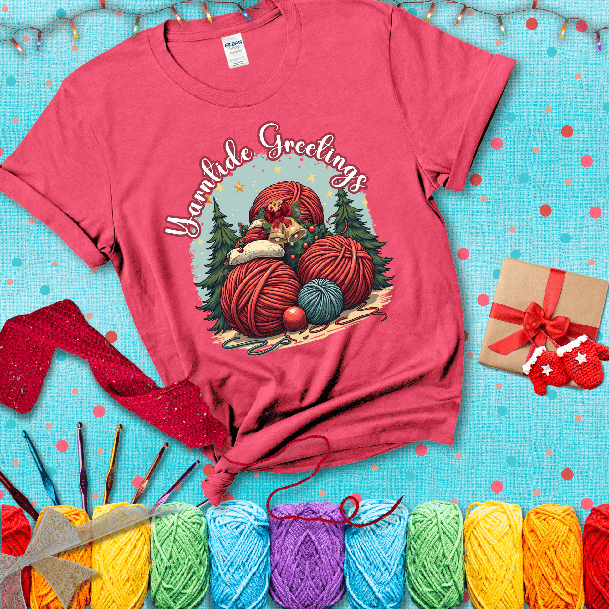 Pile of colorful yarn balls with bells, bows, and trees, with the phrase “Yarntide Greetings.” Cozy and festive holiday crochet tee, showing a light red tee with a festive Christmas background