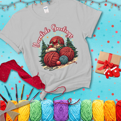 Pile of colorful yarn balls with bells, bows, and trees, with the phrase “Yarntide Greetings.” Cozy and festive holiday crochet tee, showing a light grey tee with a festive Christmas background