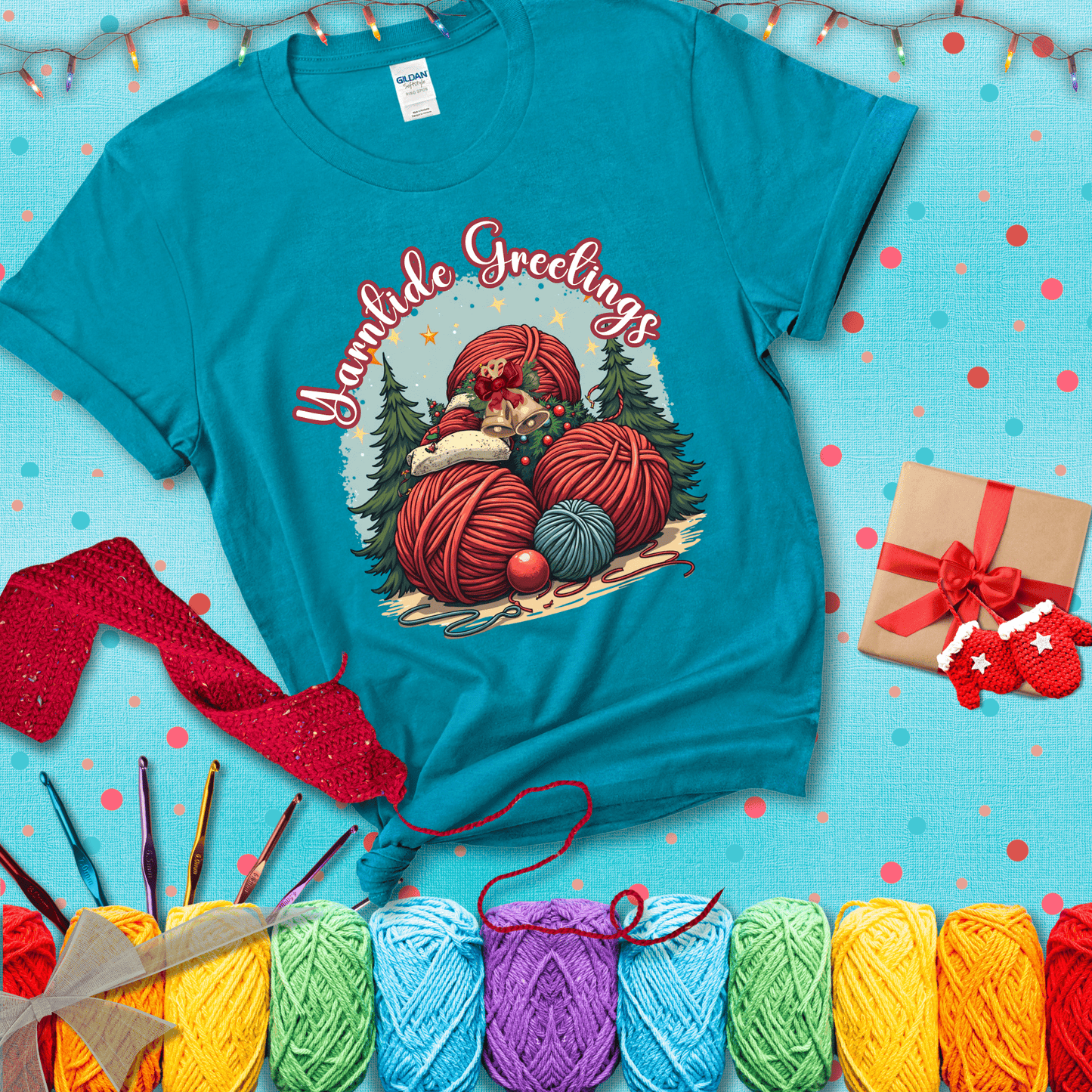 Pile of colorful yarn balls with bells, bows, and trees, with the phrase “Yarntide Greetings.” Cozy and festive holiday crochet tee, showing a blue-green tee with a festive Christmas background