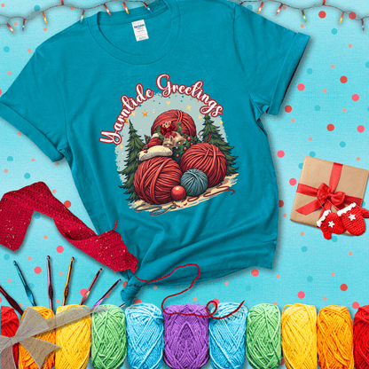 Pile of colorful yarn balls with bells, bows, and trees, with the phrase “Yarntide Greetings.” Cozy and festive holiday crochet tee, showing a blue-green tee with a festive Christmas background